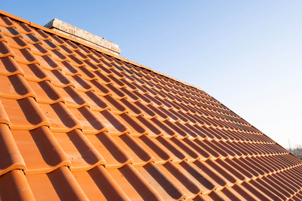 Close-up of a terracotta-colored roof with overlapping tiles in bright sunlight.