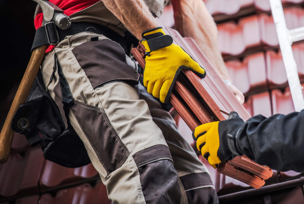 Construction worker handling roofing tiles while on a ladder.