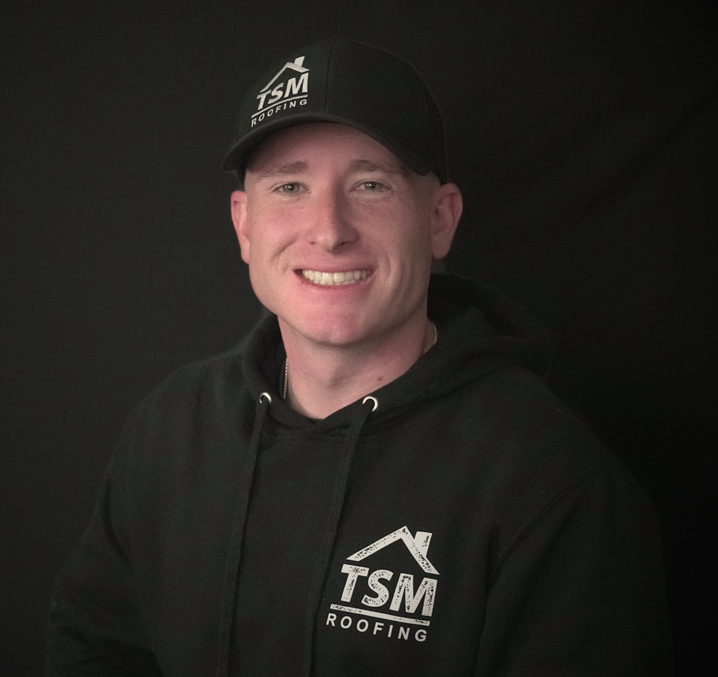 Smiling person in TSM Roofing hoodie and cap on a dark background