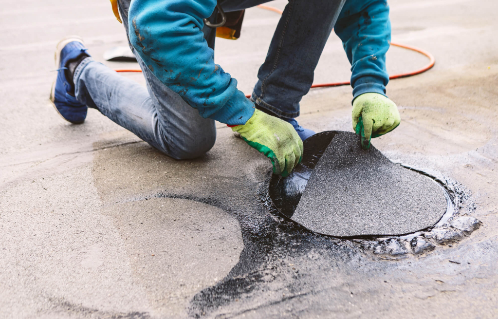 Worker repairing asphalt with patch material on road surface.