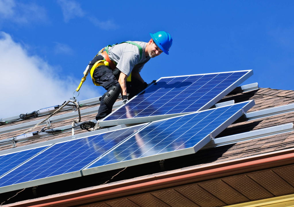 Man in safety gear installing solar panels on residential roof.