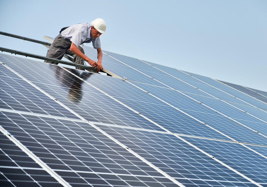 Worker installing solar panels on a roof in bright sunlight